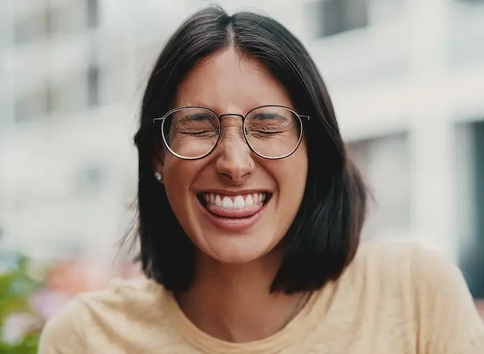 Young woman with round glasses playfully biting her tongue while smiling